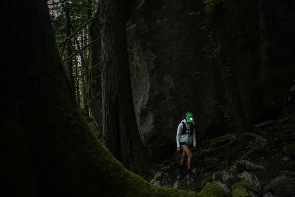 A person with a headlamp hikes through a lush forest. 