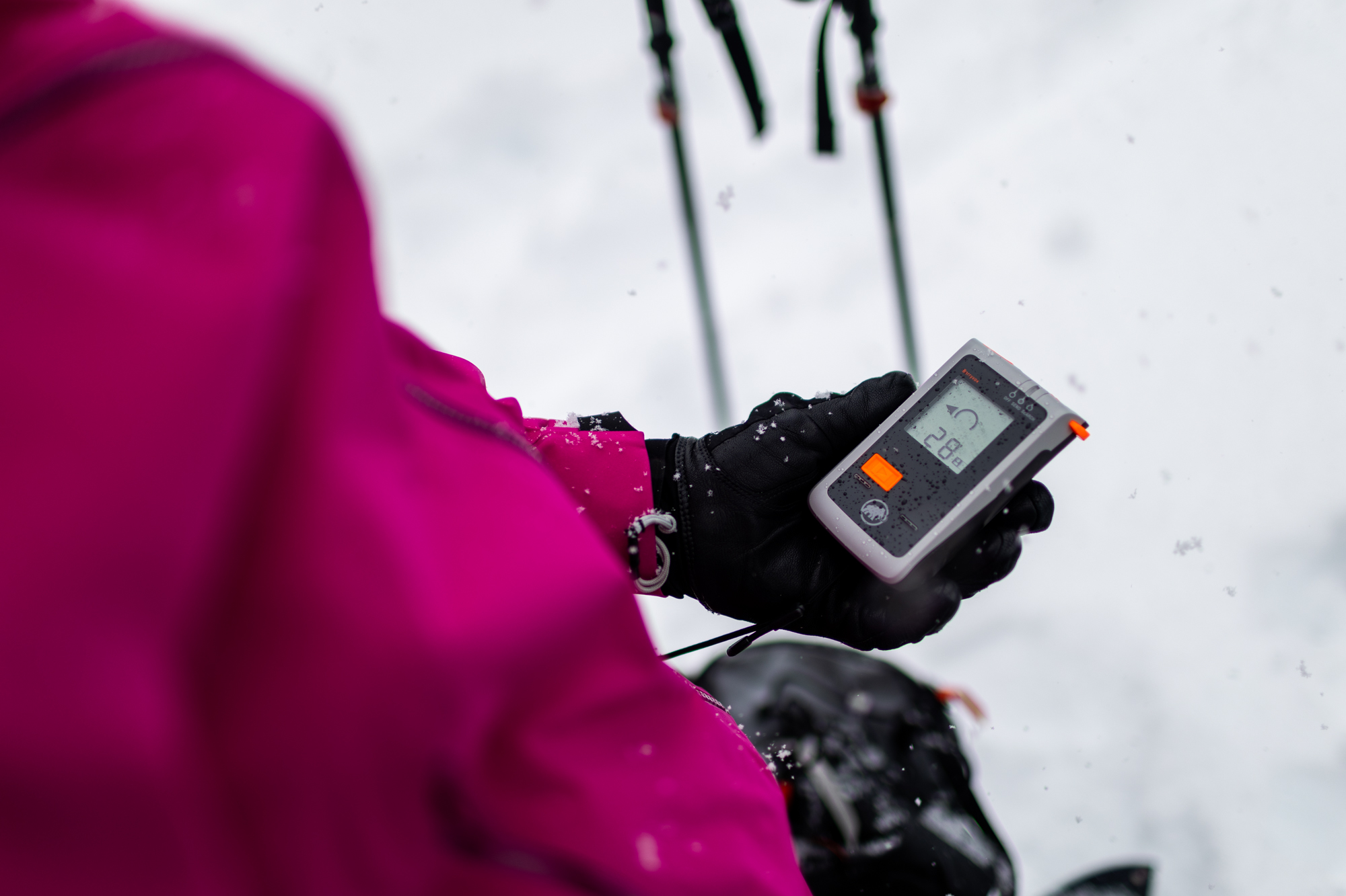 A person wearing a bright pink jacket holds an avalanche beacon. 