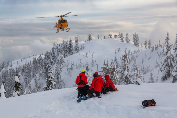 North Shore Search and Rescue helicopter flying in to a group of SAR members on a ski hill 