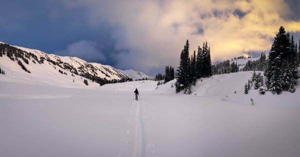 A person ski touring up a mountain with their snowy tracks behind them. 